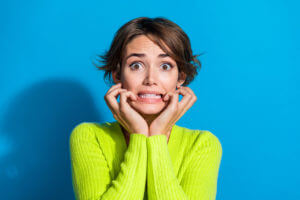 A photo of a worried person with hands on cheeks, grinning due to anxiety.