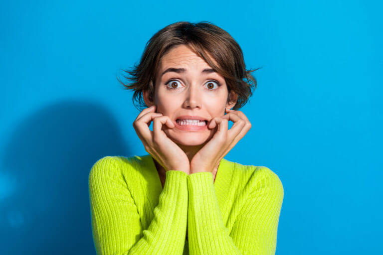 A photo of a worried person with hands on cheeks, grinning due to anxiety.