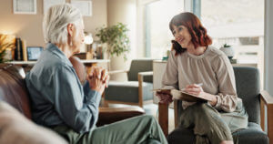 A female psychiatrist chats with a senior woman, taking notes and smiling during a mental health assessment in consultation.